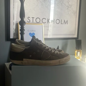 Gråa sneakers från Philippe Model - Säljer ett par gråa Philippe Model sneakers med vita detaljer och platt sula. Skorna har snörning och är tillverkade i skinn och syntet. Perfekta för dig som gillar stilrena och klassiska sneakers. Strl 41 men passar 42 