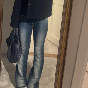 Blå, low waist, bootcut jeans med slitningar - Säljer ett par blå bootcut jeans med snygga slitningar och tvättade detaljer. Jeansen har normal passform och klassisk femficksdesign. Perfekta för dig som gillar en tidlös och avslappnad stil.