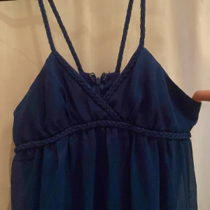 Mörkblå långklänning med flätade axelband - Säljer en elegant mörkblå långklänning med smala, flätade axelband och v-ringad hals. Klänningen har en luftig passform och markerad midja med flätad detalj. Perfekt för sommarens tillfällen ellr bal! 👌