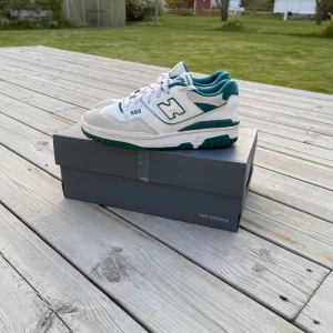 New Balance 550 vita och gröna sneakers - Säljer ett par New Balance 550 sneakers i vitt och grönt med klassisk retrodesign. Skorna har snörning, rund tå och platt sula. Perfekta för dig som gillar streetwear och vill ha en stilren look med en sportig touch.