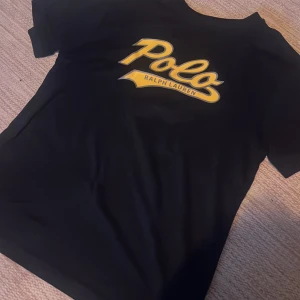 Marinblå t-shirt från Polo Ralph Lauren - Säljer denna snygga Ralph lauren T-shirten då den är för liten. Den är nästan helt oanvänd och därför i nyskick. Den är i lite stretchigt material vilket gör den väldigt skön. Den är i storlek 14-16 och passar ca 160-170 cm bra.
