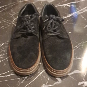 Svarta mocka loafers från Gant - Säljer ett par svarta loafers från Gant i mocka med rund tå och platt sula. Skorna har snörning och en diskret logga på sidan. Perfekta för en stilren och avslappnad look.