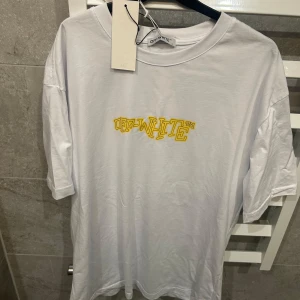 Vit t-shirt från Off-White med gul grafik - Vit t-shirt från Off-White med gul textlogga framtill och stor grafisk illustration i gult och svart på ryggen. Klassisk passform och rund halsringning. Perfekt för dig som gillar streetwear och unika prints.