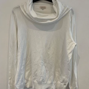 Vit polotröja från Cappuccini - Säljer en vit långärmad polotröja från Cappuccini i mjukt bomullsmaterial. Tröjan har en bred polokrage och ribbade muddar vid ärmslut och nederkant. En liten silverfärgad detalj finns på ena ärmen.