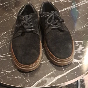 Svarta mockaskor med snörning - Säljer ett par svarta mockaskor från Cavani med klassisk snörning och rund tå. Skorna har en platt sula i brunt och passar perfekt till en stilren look. Enkla att matcha med olika outfits.
