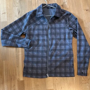 Helt ny Rutig overshirt från Jack & Jones - Snygg rutig overshirt från Jack & Jones i grå och bruna toner. Jackan har dragkedja framtill, klassisk krage och långa ärmar med knapp vid ärmslut. Perfekt för lager-på-lager-stil under höst och vår. Aldrig används