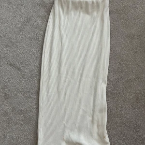 Vit ribbad långkjol från Pull&Bear - Säljer en vit ribbad långkjol från Pull&Bear. Kjolen har en smal passform och är tillverkad i ett stretchigt material med diskreta vertikala ränder. Perfekt för en stilren och enkel look.