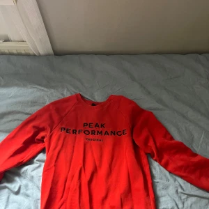 Röd sweatshirt från Peak Performance - Säljer en röd sweatshirt från Peak Performance med svart text på bröstet. Tröjan har rund halsringning och långa ärmar. Perfekt för en stilig och avslappnad stil.