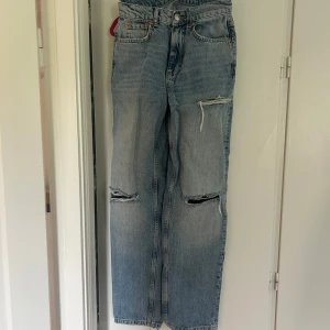 Ljusblå slitna jeans med raka ben - Ljusblå jeans från Gina Tricot med raka ben och flera slitningar på framsidan. Klassisk femficksmodell som är midwaist. Jeansen har en avslappnad passform och är perfekta för en cool och snygg outfit.
