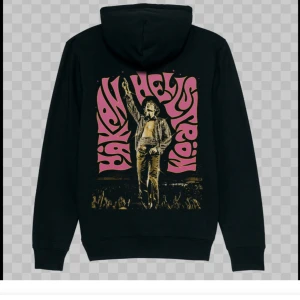 Svart Håkan Hellström hoodie - Svart hoodie med tryck av Håkan Hellström i rosa och gult på ryggen och mindre logga på bröstet. Klassisk huva och känguruficka framtill. Perfekt för dig som vill visa din kärlek till Håkan! Den är ifrån live 2023