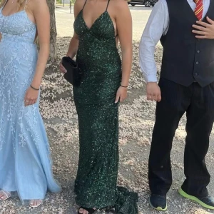 Grön glittrig långklänning med öppen rygg - NYPRIS 5000, säljer för 1500 för vill bli av med den. BILDERNA ÄR MINA! Säljer en elegant grön långklänning med glittrigt tyg och djup v-ringning. Klänningen har smala axelband som korsas i ryggen och en öppen rygg för en snygg look. Perfekt för bal eller fest! 💚