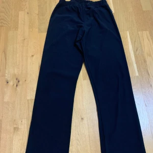 Svarta mjukisbyxor från CHNK - Svarta mjukisbyxor från CHNK med resår i midjan och raka ben. Byxorna är tillverkade i ett mjukt och bekvämt material, perfekta för en avslappnad stil. Klassisk design utan synliga detaljer eller mönster.