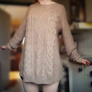 Beige stickad oversized tröja med flätmönster - Mysig beige stickad tröja med snyggt flätmönster och diamantstruktur både fram och bak. Tröjan har långa ärmar och en oversized passform, perfekt för lager-på-lager och chill dagar.