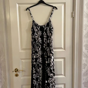 Svart långklänning med vita blommor - Säljer en svart långklänning med vita blommor och smala axelband.Mönstret är tropiskt och ger en somrig känsla. Ingen direkt storlek så den är Onesize🖤🤍några trådar behövs däremot sys fast.