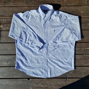 Blåvit randig skjorta från Ralph Lauren - 📊 Färg: Vit & Ljusblå  📏 Storlek: Extra Large (XL)  📐 Mått: Längd - 84cm Axelbredd - 56cm  ♻️ En långärmad Vit och blå Ralph lauren skjorta i storlek XL, det står att den är i XXL men den är mycket mer som XL. I väldigt bra skick. Inga fläckar, hål eller defekter! Perfekt nu när det börjar bli varmare och sommaren kommer!☺️  👕 Material: 100% Bomull