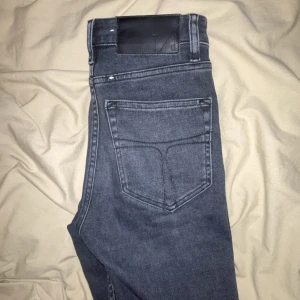 Grå jeans från Tiger of Sweden - Säljer ett par grå jeans från Tiger of Sweden med klassisk femficksdesign och raka ben. Jeansen har en svart patch bak i midjan och diskreta sömmar. Perfekta för dig som gillar stilrena och tidlösa jeans. Helt nya 