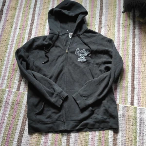 Svart hoodie med dragkedja från Fruit of the Loom - Säljer en svart hoodie med dragkedja från Fruit of the Loom. Tryck med texten 'Smith's Burgers' och en städ på både bröstet och ryggen. köpte den secondhand där av lite fläckig. Tröjan är ganska liten i storleken passar både dam M och Herr L