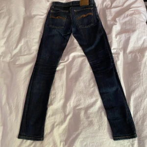 Nudie Jeans - Säljer ett par mörkblå jeans från Nudie Jeans med klassisk femficksdesign.Storlek W26 L32