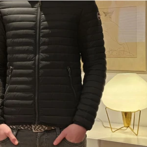 Svart pufferjacka från Colmar - Säljer en svart pufferjacka från Colmar med horisontella sömmar och dragkedja framtill. Jackan har lång ärm, två fickor med dragkedja och en diskret logotyp på ärmen. Perfekt för kyliga dagar.