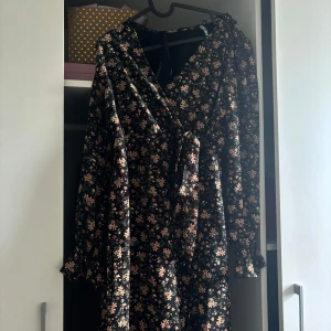 Svart blommig omlottklänning - Svart långärmad omlottklänning med små blommor i orange och beige. Klänningen har knyt i midjan och v-ringad hals. Perfekt för dig som gillar romantiska detaljer och blommigt mönster.storlek xs från pieces. 