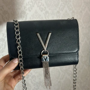 Svart axelväska med silverdetaljer från Valentino Bags - Snygg svart axelväska med grov silverkedja och dekorativt V i metall framtill. 