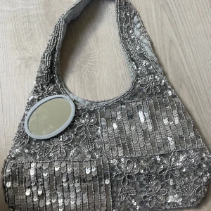 Glittrig väska - Den perfekta festväskan! Glittrig med broderade paljetter och pärlor. Även tillhörande liten spegel som sitter fast i väskan💫