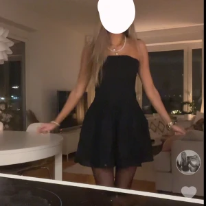 Svart axelbandslös klänning - Säljer en svart axelbandslös klänning med utställd kjol. Klänningen har en enkel och stilren design som ger en klassisk look. Perfekt för dig som gillar minimalistisk stil och vill ha något tidlöst i garderoben.