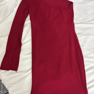 Röd ribbad långärmad klänning - Snygg röd ribbad klänning med lång ärm och asymmetrisk halsringning. Modellen är tight och kort. Materialet är stretchigt och följsamt, vilket gör den superbekväm att bära. Endast använd 2 gånger. 