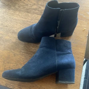 Mörkblå mocka stövletter med klack - Snygga mörkblå stövletter i mocka med rund tå och låg klack. Skorna har dragkedja på insidan för enkel påtagning och en stilren, minimalistisk look. Perfekta för dig som gillar klassiska boots med en modern twist.