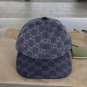Blå GG-monogram keps från Gucci - Snygg blå keps från Gucci med ikoniskt GG-monogram över hela ytan. Kepsen har böjd skärm, justerbar rem bak och är tillverkad i bomullscanvas. Perfekt för dig som vill sticka ut med en lyxig accessoar och visa din stil.