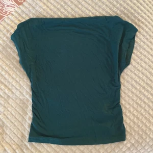 Mörkgrön topp med öppen rygg - Snygg mörkgrön topp i mjukt material med korta ärmar och en öppen rygg. Toppen har en rak passform och är lätt att matcha med både jeans och kjol.