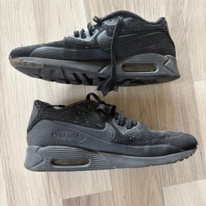 Svarta Nike Air Max sneakers - Svarta Nike Air Max sneakers med klassisk synlig luftbubbla i sulan. Skorna har snörning, rund tå och är tillverkade i syntetmaterial med små prickdetaljer över hela ovandelen. Perfekta för dig som gillar en sportig och stilren look.