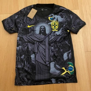 Nike Brasil Dri-Fit fotbollströja M - Snygg svart och grå Brasilien fotbollströja från Nike med unikt tryck av Kristusstatyn och brasilianska motiv. Tröjan har korta ärmar, gula detaljer och är tillverkad i Dri-Fit material som andas. Perfekt för dig som vill sticka ut på planen eller läktaren.