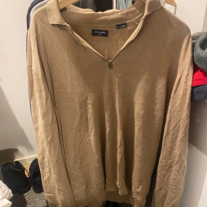 Beige stickad tröja Jack & Jones L - Beige stickad tröja från Jack & Jones med krage och half zip-dragkedja. Tröjan har lång ärm och en klassisk, avslappnad passform. Perfekt för lager-på-lager och enkel att matcha med jeans eller chinos.