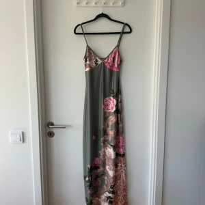 Lång blommig klänning med smala axelband - Supersnygg långklänning med smala axelband och blommigt mönster i rosa, grönt och beige på en dov grågrön bas. Klänningen är från SHEIN och är helt nt och oanvänd! 