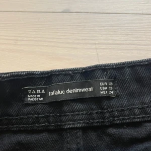 Svart jeanskjol från Zara XS - Säljer en svart jeanskjol från Zara i modellen 'rafaluc denimwear'. Kjolen har rå kant nertill, klassiska fem fickor och bälteshällor. Snygg och enkel att styla med allt, perfekt för dig som gillar en edgy vibe.