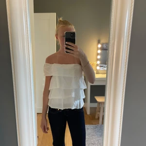 Vit volangig offshoulder topp - Säljer en superfin vit offshoulder topp med flera lager volanger. Toppen är axelbandslös och har en luftig, flowy känsla som passar perfekt till jeans eller kjol. Materialet känns lätt och somrigt, perfekt för varma dagar.