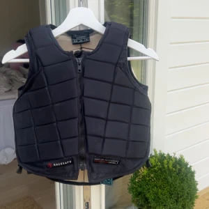 Svart skyddsväst från Racesafe - Säljer en svart quiltad skyddsväst från Racesafe, perfekt för ridning. Västen har dragkedja framtill, rutmönstrad vaddering och justerbara sidor med snörning. 