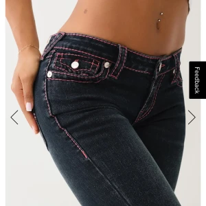True Religion jeans med rosa sömmar - Mörkblå jeans från True Religion med ikoniska bakfickor och kontrasterande rosa sömmar. Låg midjade.