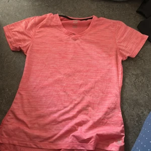 Rosa tränings-tshirt från SOC - Sportig rosa t-shirt från SOC med v-ringning och korta ärmar. Tillverkad i lätt och ventilerande syntetmaterial, perfekt för träning. Snyggt melerat mönster och reflexdetalj på ryggen för extra synlighet.
