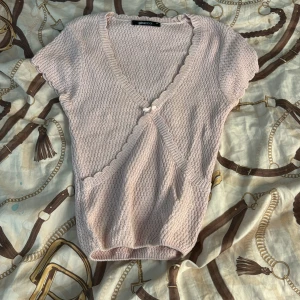 Ljusrosa omlottstickad topp Gina Tricot - Supersöt ljusrosa stickad topp från Gina Tricot i omlottmodell med korta ärmar och v-ringning. Söt liten rosett framtill och vågig kant längs ringningen. Perfekt till vår och sommar för en gullig och trendig look. Inga difekter och använd fåtal gånger. DM vid intresse💕