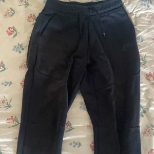 Svarta mjukisbyxor från Nike - Passar folk som är mellan 158-170cm.Svarta mjukisbyxor från Nike med dragsko i midjan och två sidofickor. Byxorna har en relaxed passform och är tillverkade i mjukt bomullsmaterial. Perfekta för chill eller träning. Diskret Nike-logga på låret.