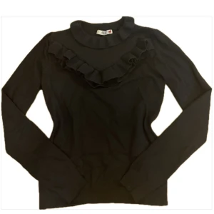 Svart volangtröja från Dilvin - Stickad svart långärmad tröja från Dilvin med snygga volangdetaljer framtill. Perfekt om du vill ha något lite finare än en basic stickad tröja. Passar XS/S. 