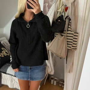 Svart stickad half zip från Noisy May - Svart stickad tröja från Noisy May med half zip och rund dragkedja i silver. Tröjan har lång ärm och en lite loose passform, perfekt till jeans eller kjol. Enkel och stilren design som funkar året runt.