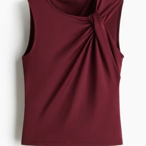 Vinröd ärmlös topp med knutdetalj - Säljer en vinröd ärmlös topp i stl xs med snygg knutdetalj vid axeln. Toppen har enkla men coola detaljer.