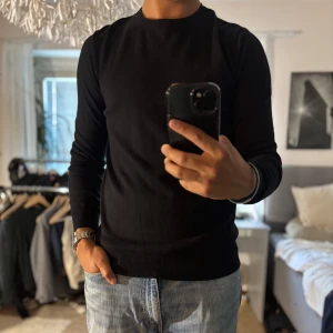 Svart tröja i pima bomull, Dressmann M - Klassisk svart tröja från Dressmann i mjuk pima bomull. Enkel rund halsringning, ribbade muddar och lång ärm. Perfekt till jeans eller chinos för en clean och stilren look.