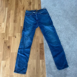 Blå Lee Jeans 32/34 - Klassiska blå jeans från Lee med raka ben och normal passform. Jeansen har fem fickor, snygga kontrastsömmar och Lee-lapp bak i midjan. Perfekta för dig som gillar en tidlös look och vill ha ett par jeans som funkar till allt. Skick 10/10.
