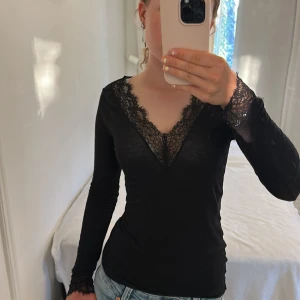 Svart långärmad spetsblus - Svart långärmad blus med djup v-ringning och snygga spetsdetaljer längs halsringningen och vid ärmsluten. Toppens passform är slim och materialet känns mjukt och följsamt. Perfekt att styla med jeans eller kjol för en trendig look. Den här är lite för stor för mig så därför jag säljer den.❤️