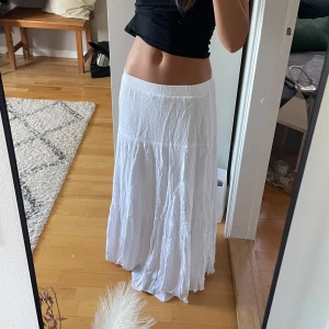 Vit långkjol med resårmidja - Säljer en flowy vit långkjol med resår i midjan. Kjolen har en lätt skrynklig struktur och faller snyggt ner mot golvet. Perfekt för varma dagar och ger en chill boho-vibe. Superenkel att matcha med crop tops eller linnen.