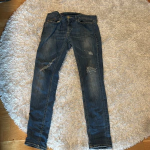Ljusblå slimfit jeans från Dondup - Säljer ett par blå slim fit jeans från Dondup med slitna detaljer och hål på benen. Klassisk femficksmodell med snygga sömmar och läderpatch bak i midjan. Jeansen har låg midja och är tillverkade i mjukt denimtyg med stretch för skön passform. Lappade riktigt bra mellan benen, syns inte när man har på sig dem. Passar 165-170 i längden. Skick 8/10 